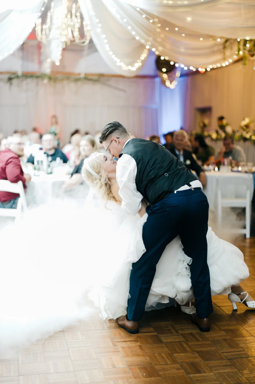 The groom dips the bride mid-laugh during their first dance as dry-ice fog rolls across the floor beneath draped fabric and string lights at Pine Peaks Event Center. — Tim Larsen Photography, Brainerd Lakes MN