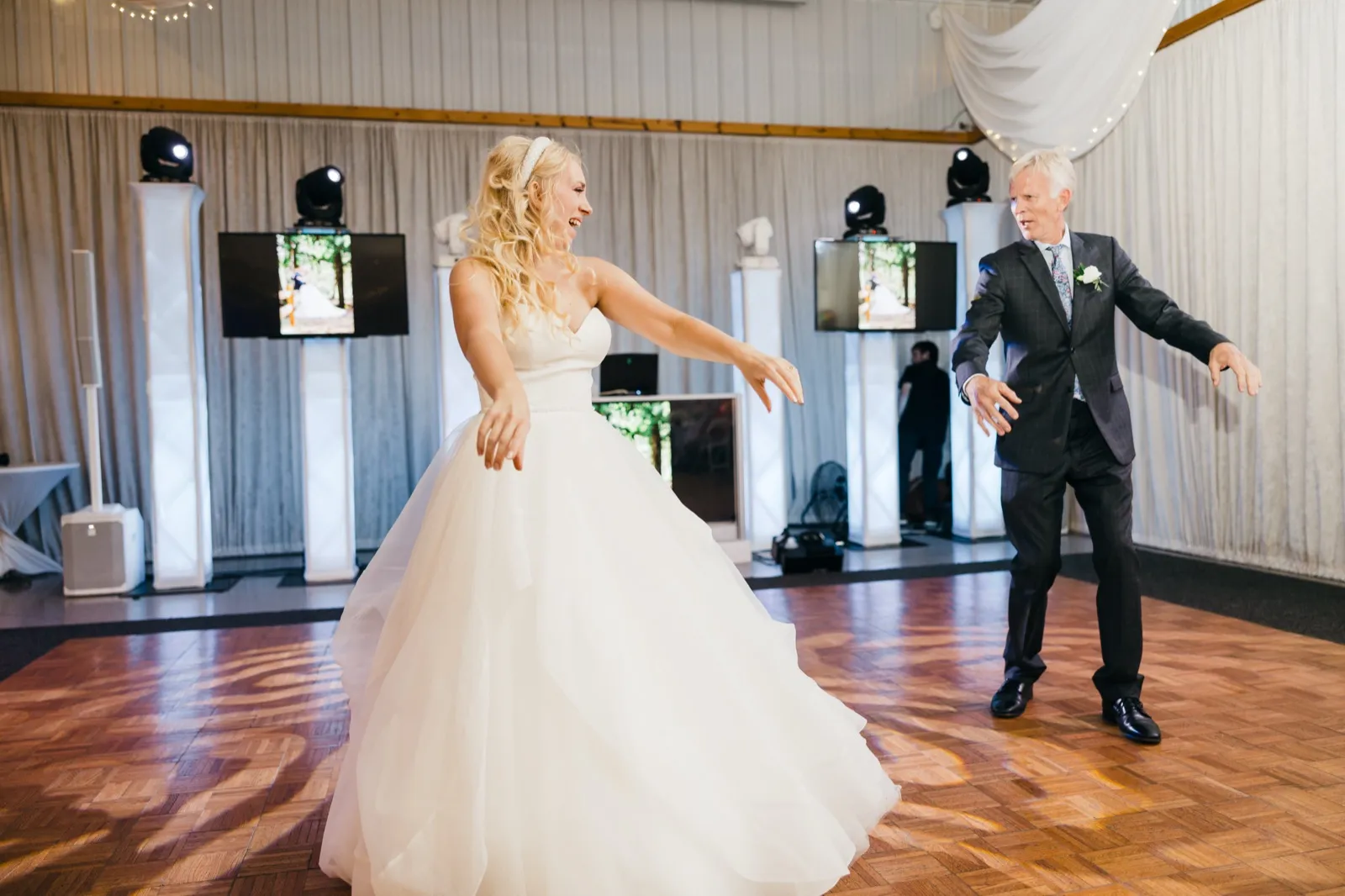 The bride laughs mid-twirl on a parquet dance floor while her father mirrors her arms-out pose during the father-daughter dance. — Tim Larsen Photography, Brainerd Lakes MN