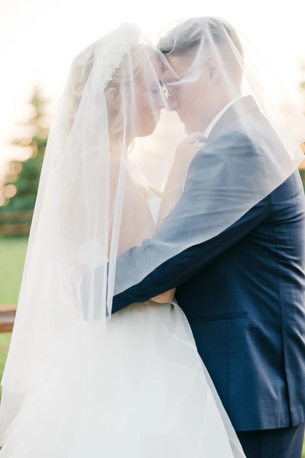 The bride and groom press their foreheads together beneath her veil, which drapes around them both in backlit evening light. — Tim Larsen Photography, Brainerd Lakes MN