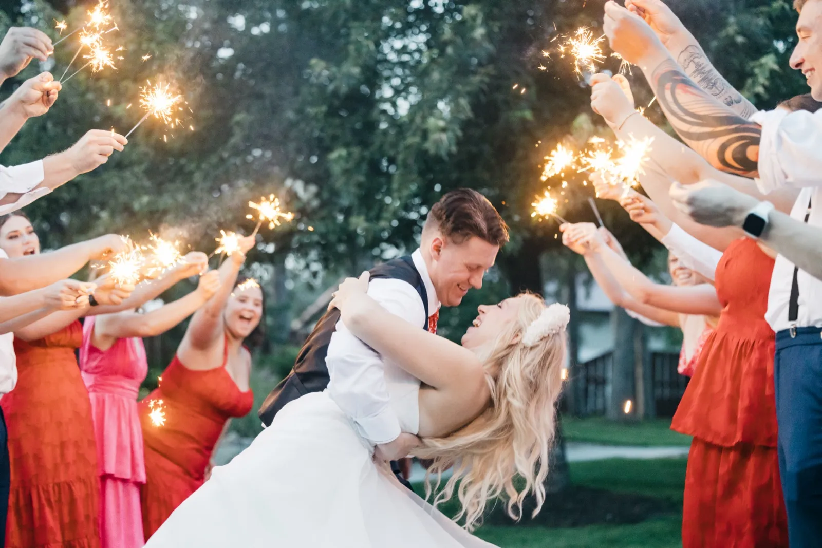 The groom dips the laughing bride at the center of a sparkler tunnel formed by their bridal party at dusk. — Tim Larsen Photography, Brainerd Lakes MN