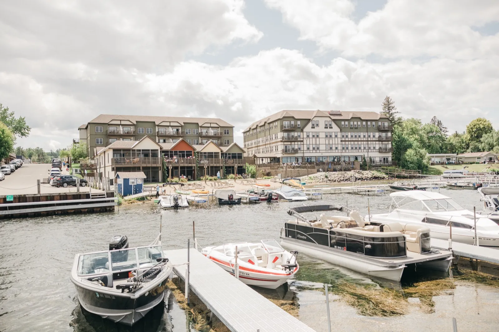 A wide view of the Chase on the Lake resort buildings rising above a marina full of moored fishing boats and pontoons under an overcast summer sky. — Tim Larsen Photography, Brainerd Lakes MN