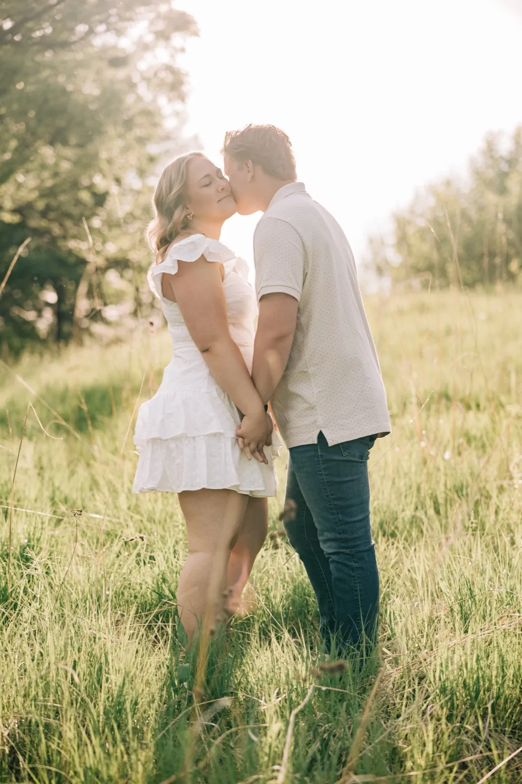 Abby and Anthony kiss in the middle of a sunlit meadow at Carver Park, hands joined between them — Tim Larsen Photography