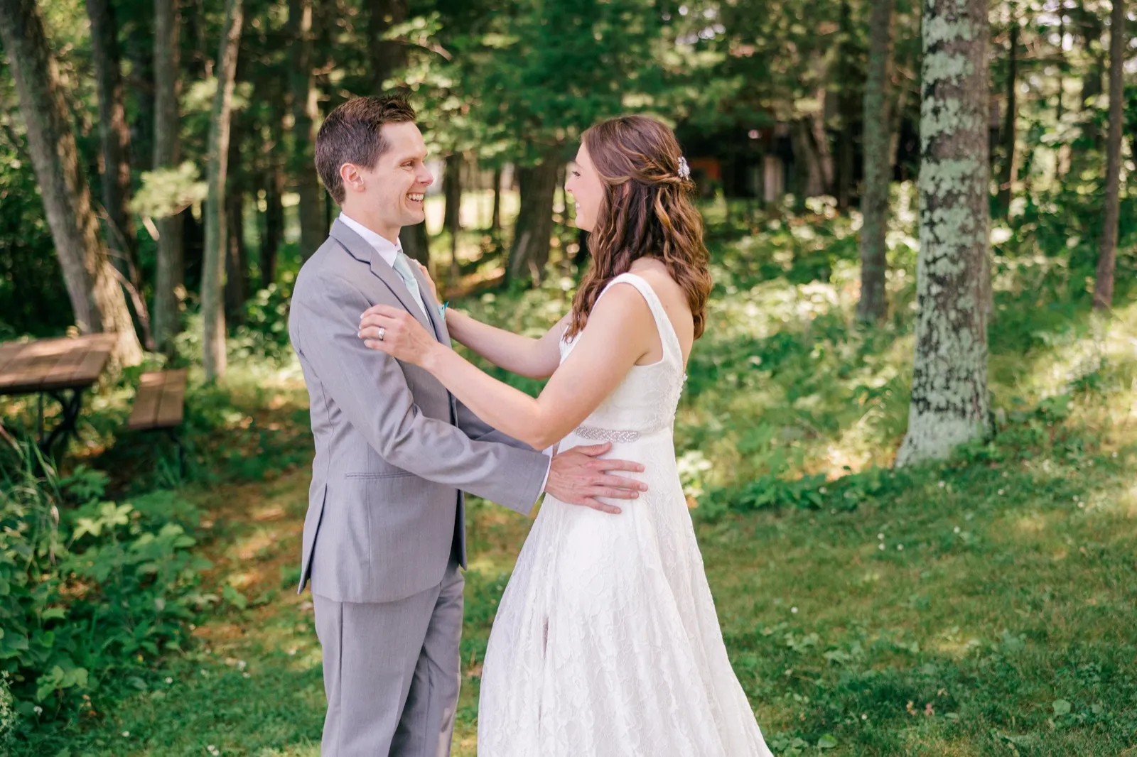 The bride and groom laugh together face-to-face in a sunlit wooded clearing, his hand resting on her back. — Tim Larsen Photography, Brainerd Lakes MN