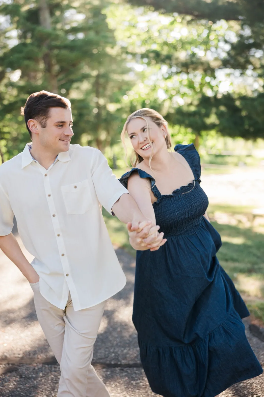A laughing engaged couple walk hand in hand across a sunlit lawn at Grand View Lodge — Tim Larsen Photography
