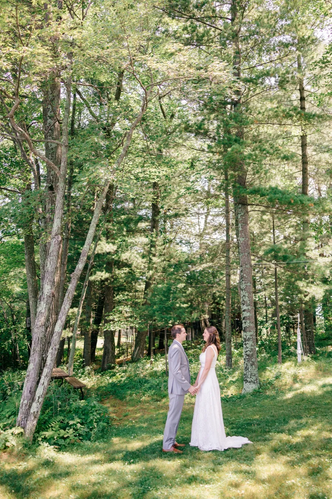 The bride and groom hold hands facing each other in a small clearing dwarfed by tall pine and birch trees. — Tim Larsen Photography, Brainerd Lakes MN