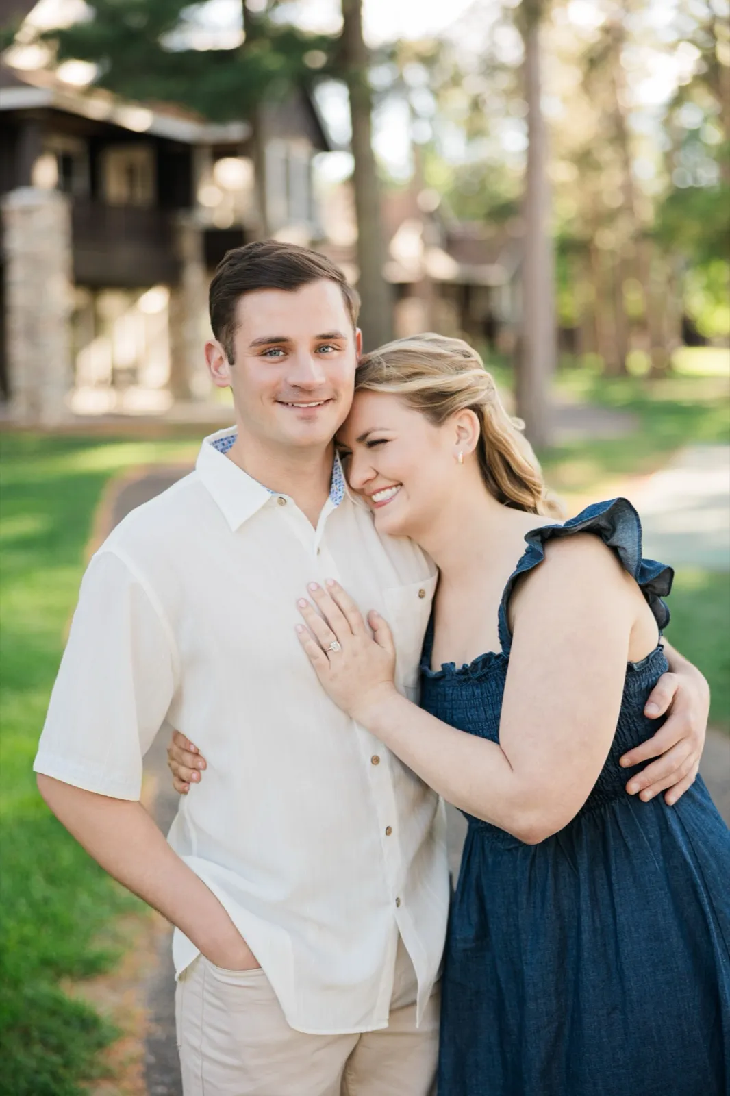 A woman nuzzles into her fiance's shoulder, her ring hand on his chest, the Roy Lake cabins behind them — Tim Larsen Photography