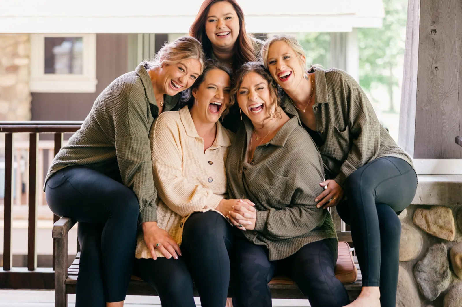 Chelsea and her three bridesmaids sit pressed together on a lodge porch bench, all laughing openly in matching neutral loungewear — Tim Larsen Photography, Brainerd Lakes MN