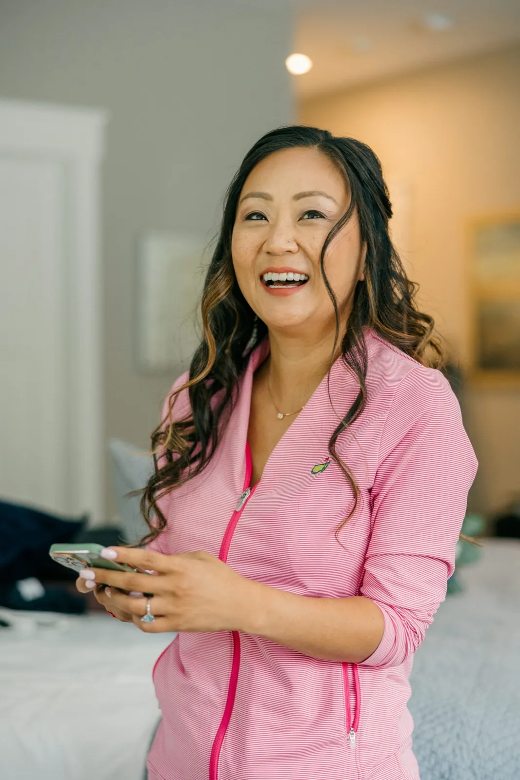 The bride laughs while holding her phone, wearing a pink striped getting-ready jacket in a softly lit bridal suite at Grand View Lodge — Tim Larsen Photography, Brainerd Lakes MN