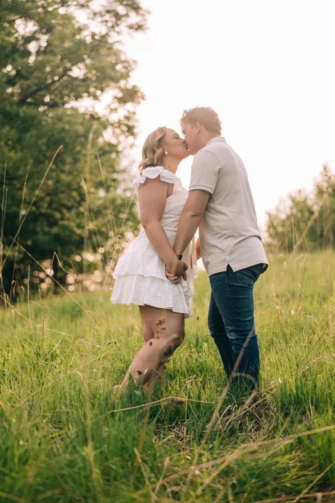 Anthony kisses Abby's cheek as she laughs, the Carver Park meadow grass glowing behind them — Tim Larsen Photography