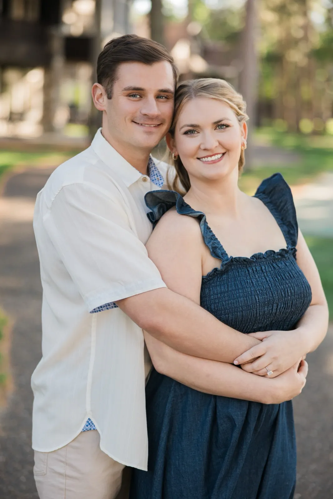 A man wraps his arms around his fiancee from behind as both smile at the camera on a resort path — Tim Larsen Photography