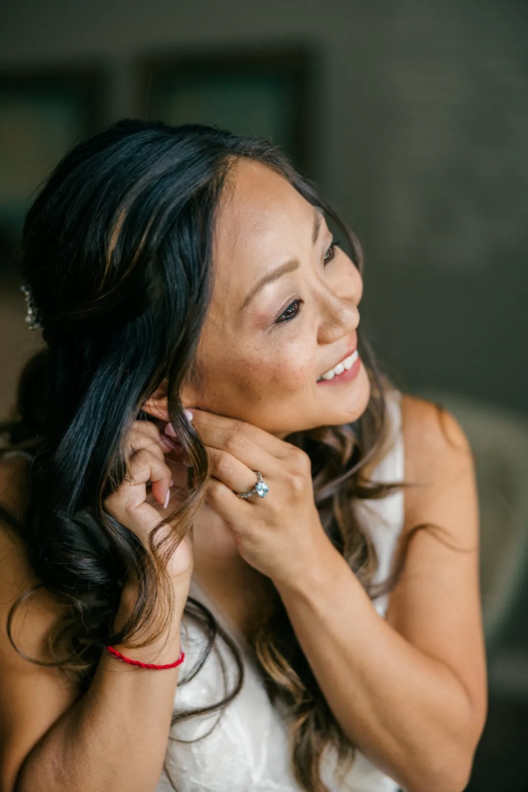 The bride smiles softly toward a window as she fastens an earring, her engagement ring visible on her hand near her jaw — Tim Larsen Photography, Brainerd Lakes MN