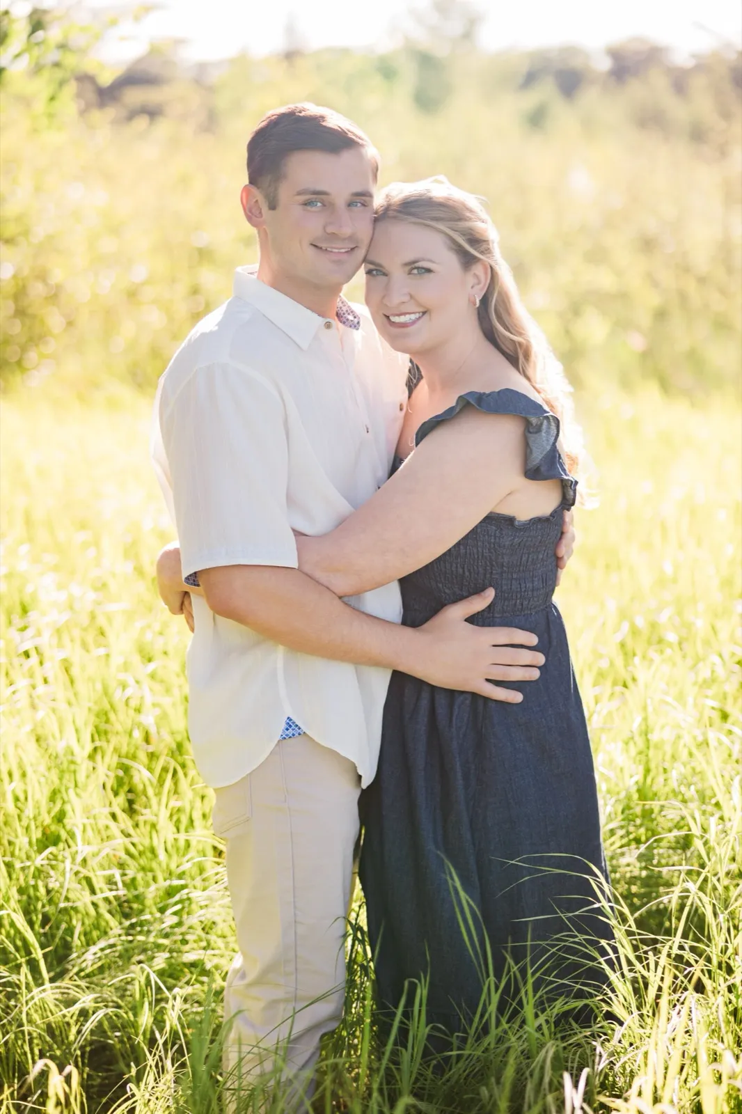 An engaged couple embrace in tall green grass on the Roy Lake side, backlit by golden evening sun — Tim Larsen Photography