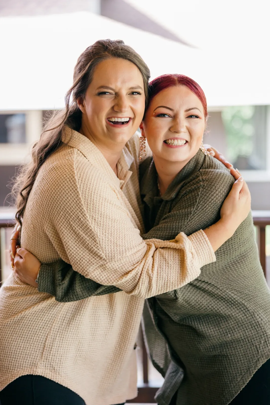 Chelsea and a bridesmaid hug tightly on a sunlit covered porch, both laughing openly toward the camera — Tim Larsen Photography, Brainerd Lakes MN