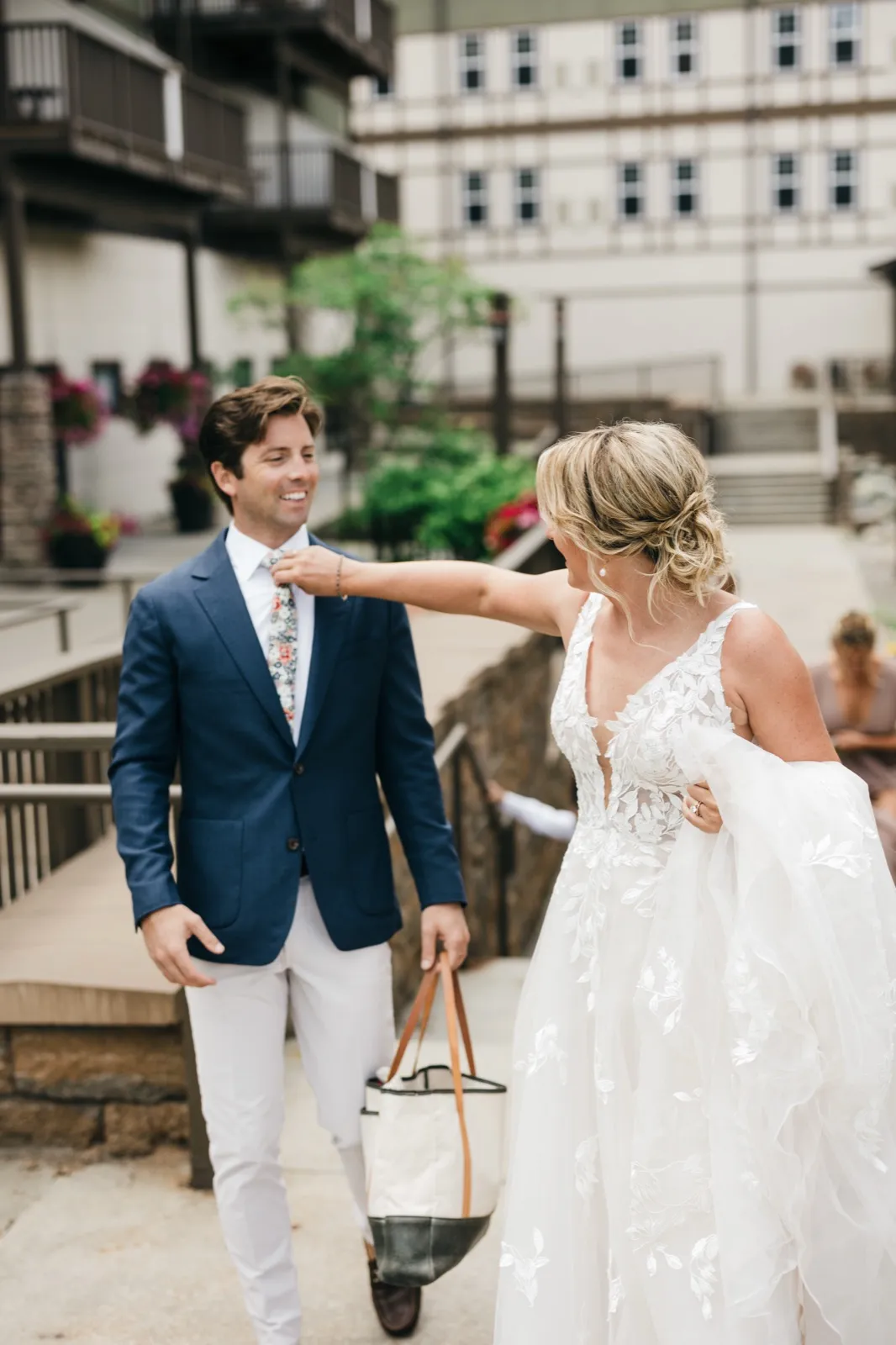 The bride reaches across to adjust the groom's tie as both laugh, walking through the Chase on the Lake courtyard. — Tim Larsen Photography, Brainerd Lakes MN