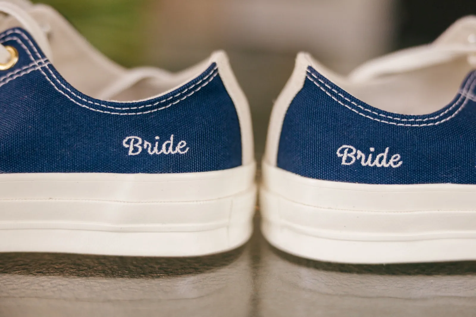A pair of navy blue canvas sneakers with 'Bride' embroidered on each heel, photographed straight-on against a soft green background — Tim Larsen Photography, Brainerd Lakes MN