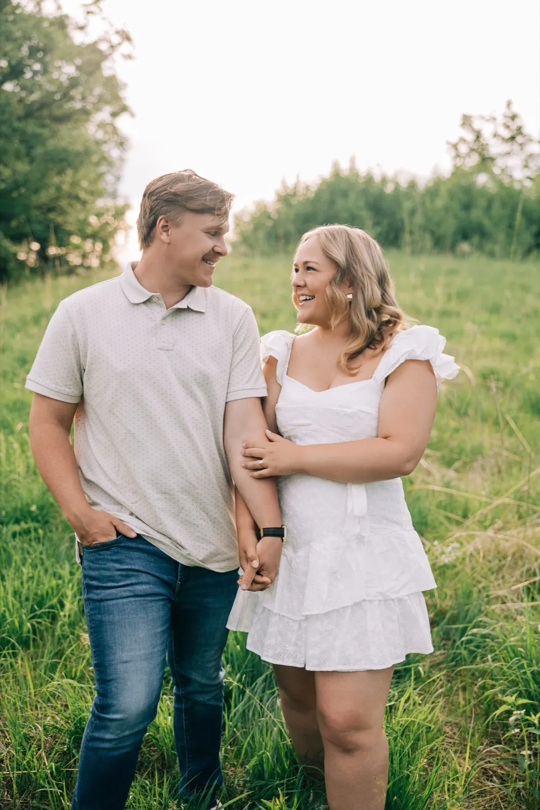 Abby and Anthony walk arm in arm through the tall grass at Carver Park, both laughing in golden light — Tim Larsen Photography