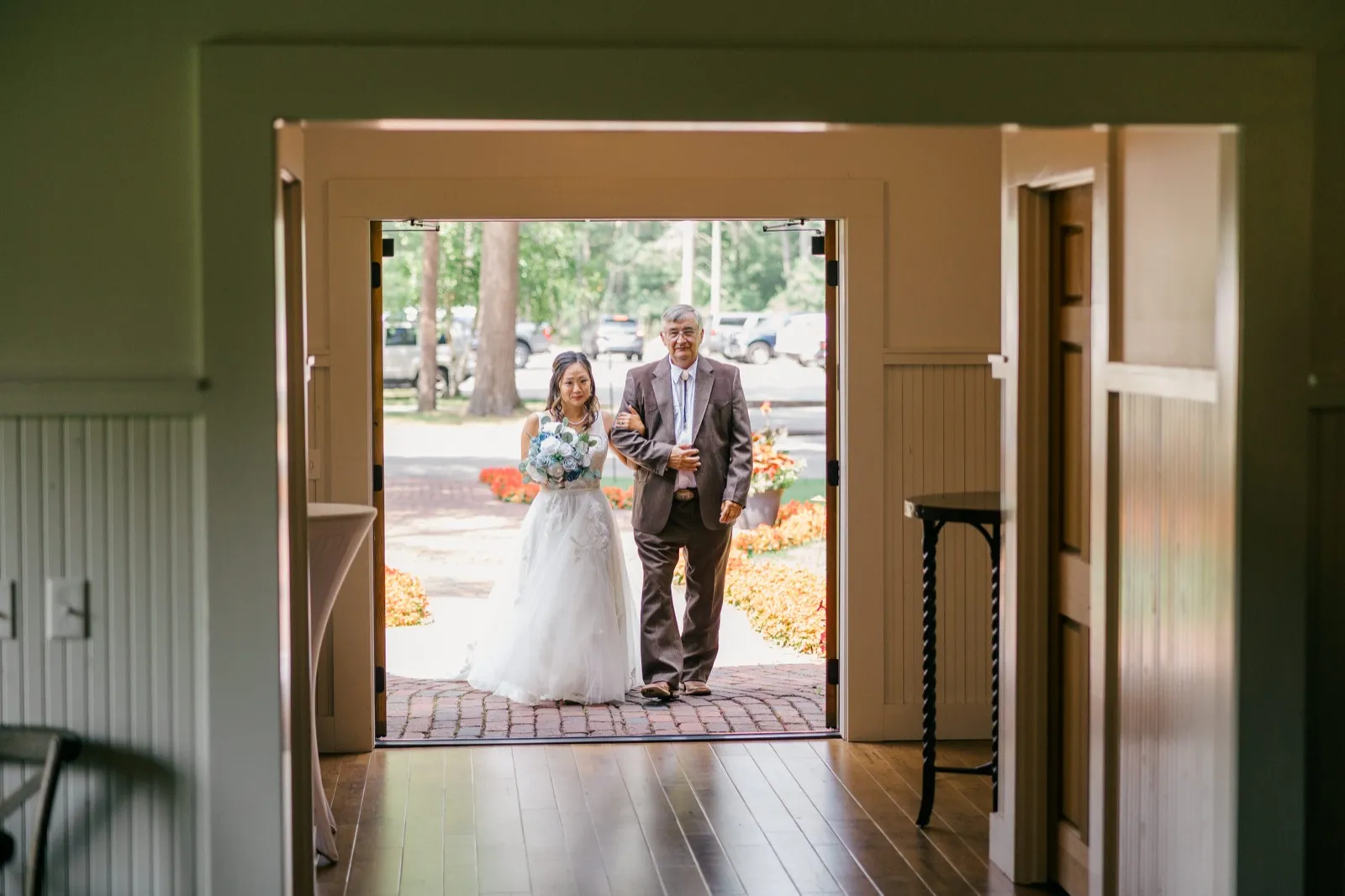 Framed through an interior doorway, the bride walks arm-in-arm with her father toward the ceremony entrance at Grand View Lodge, her bouquet held in front of her dress — Tim Larsen Photography, Brainerd Lakes MN