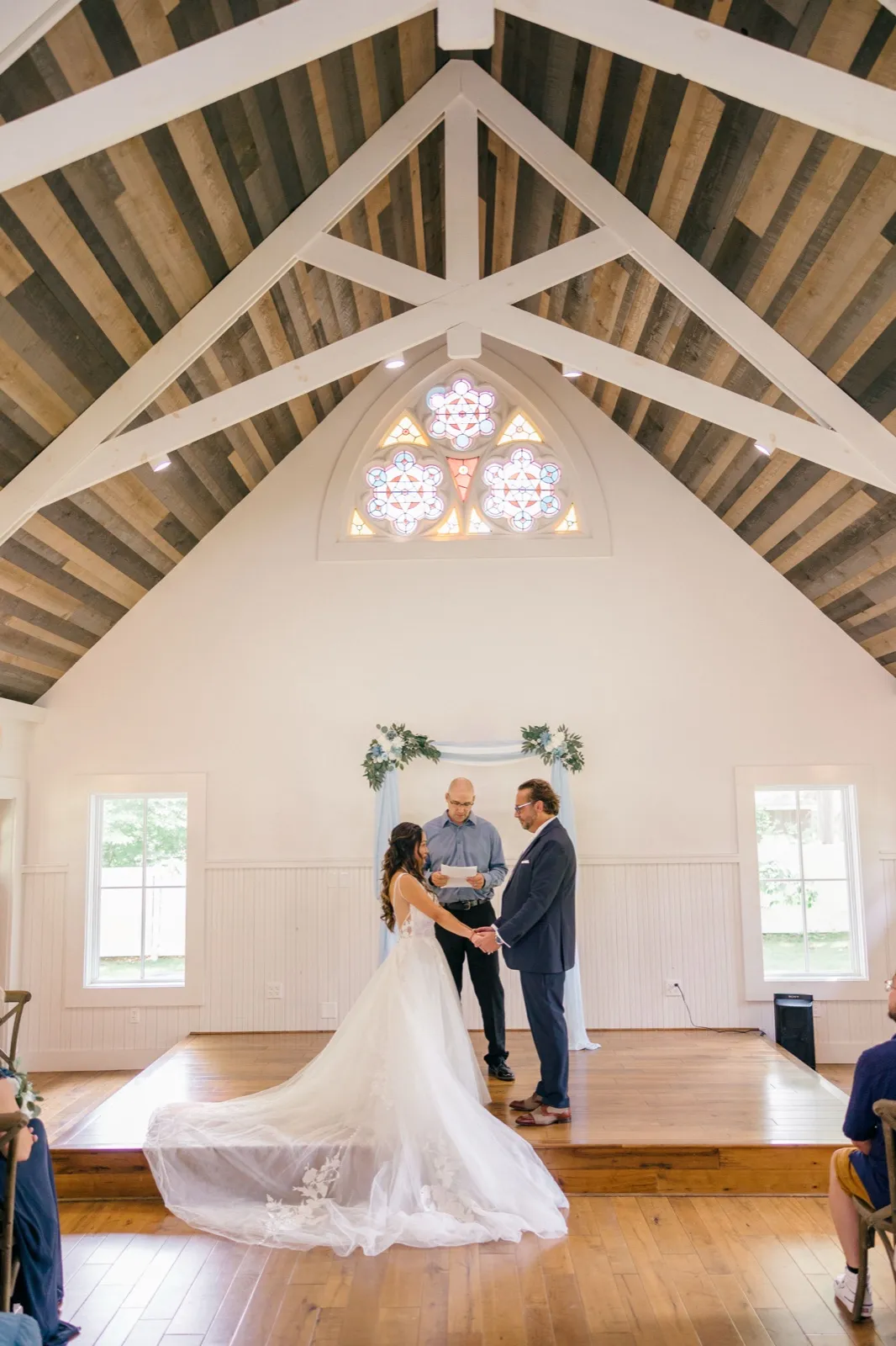 The bride and groom hold hands before the officiant beneath a vaulted wooden ceiling and stained-glass window inside the Grand View Lodge chapel — Tim Larsen Photography, Brainerd Lakes MN