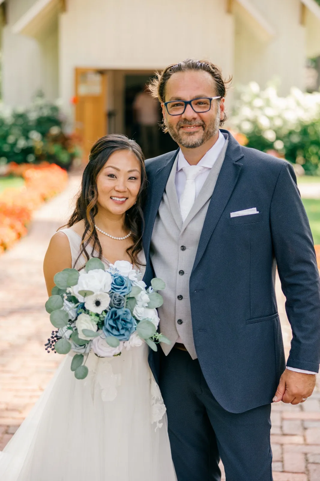 The bride and groom stand together on a brick pathway outside the chapel at Grand View Lodge, the bride holding a dusty-blue and white bouquet — Tim Larsen Photography, Brainerd Lakes MN