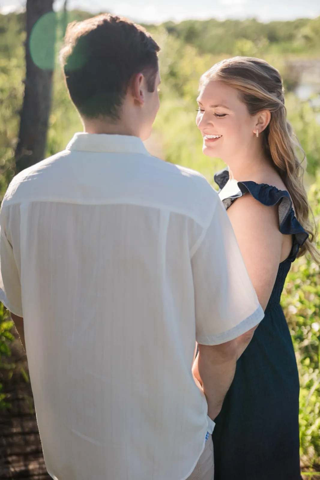 A woman laughs as she faces her fiance, whose back is to the camera, in backlit marsh grass — Tim Larsen Photography