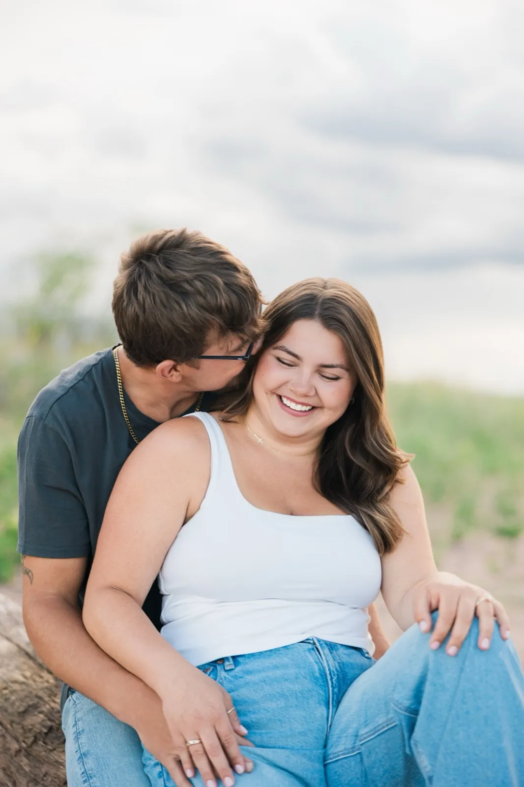 Reeden kisses Jacklyn's cheek and she laughs as they sit close together on a driftwood log — Tim Larsen Photography