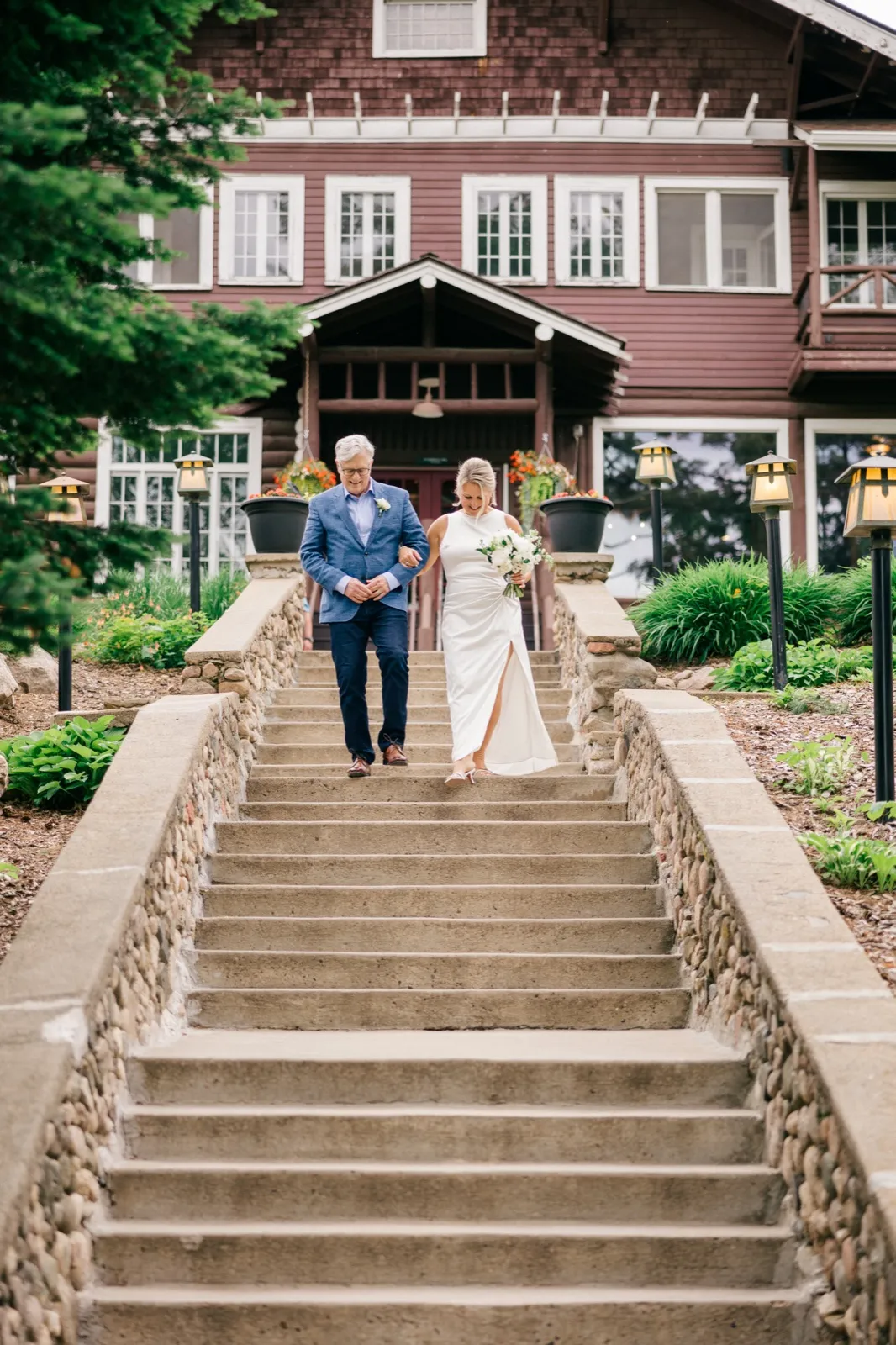 The bride and her father descend the wide stone stairway in front of the Grand View Lodge main building, her bouquet held at her side — Tim Larsen Photography, Brainerd Lakes MN