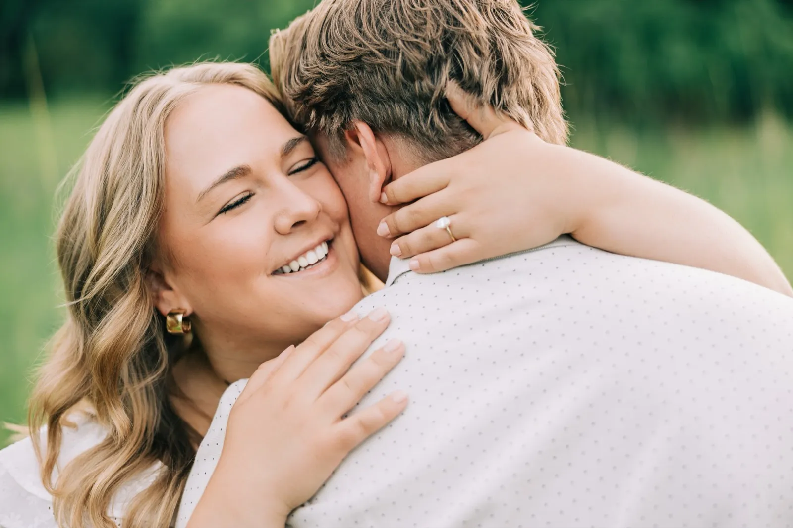 Abby smiles with her eyes closed and her arms around Anthony's neck in a sunlit meadow, her engagement ring catching the light — Tim Larsen Photography