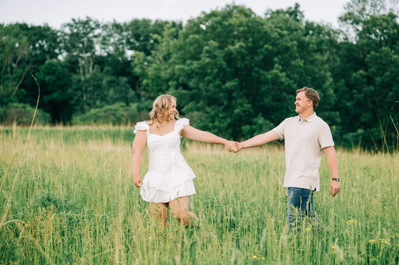Abby laughs while holding Anthony's hand at arm's length as they move through the Carver Park meadow — Tim Larsen Photography