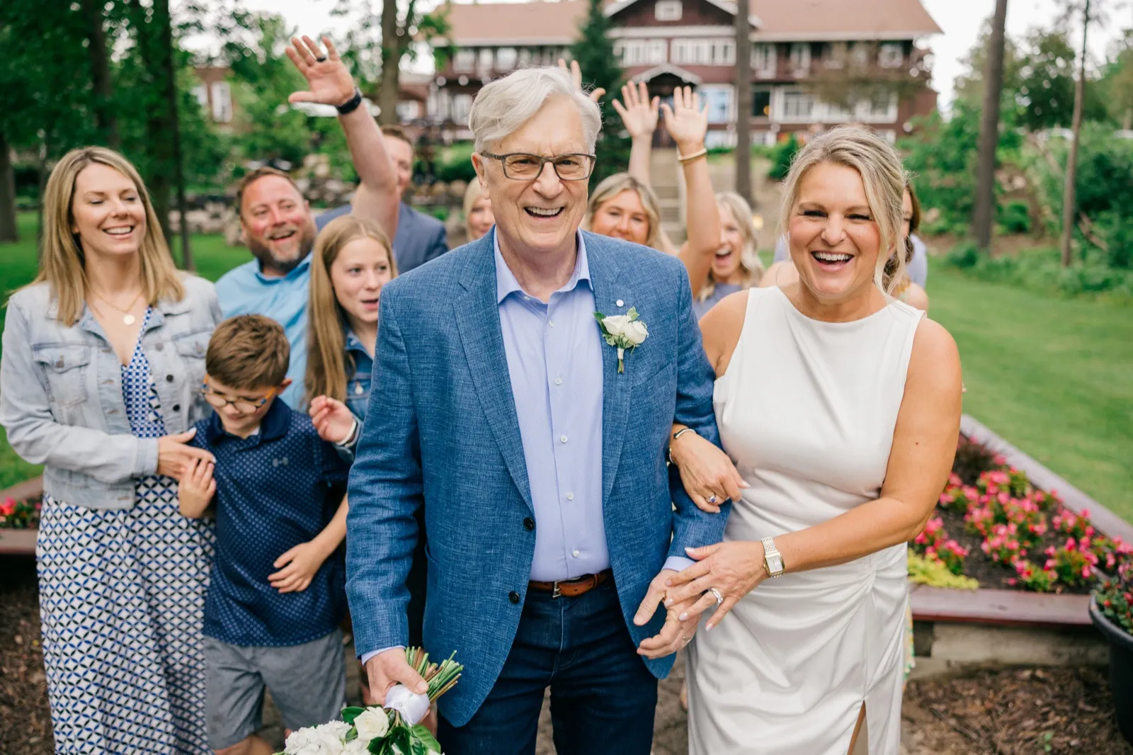 The bride and groom laugh together as family members cheer with raised arms behind them on the lawn at Grand View Lodge — Tim Larsen Photography, Brainerd Lakes MN