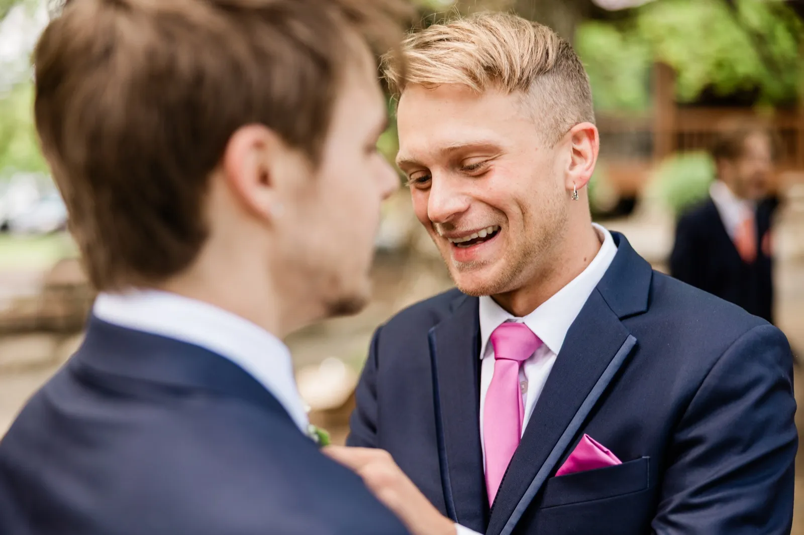 Groom laughing as a groomsman pins his boutonniere outdoors — Tim Larsen Photography, Brainerd Lakes MN