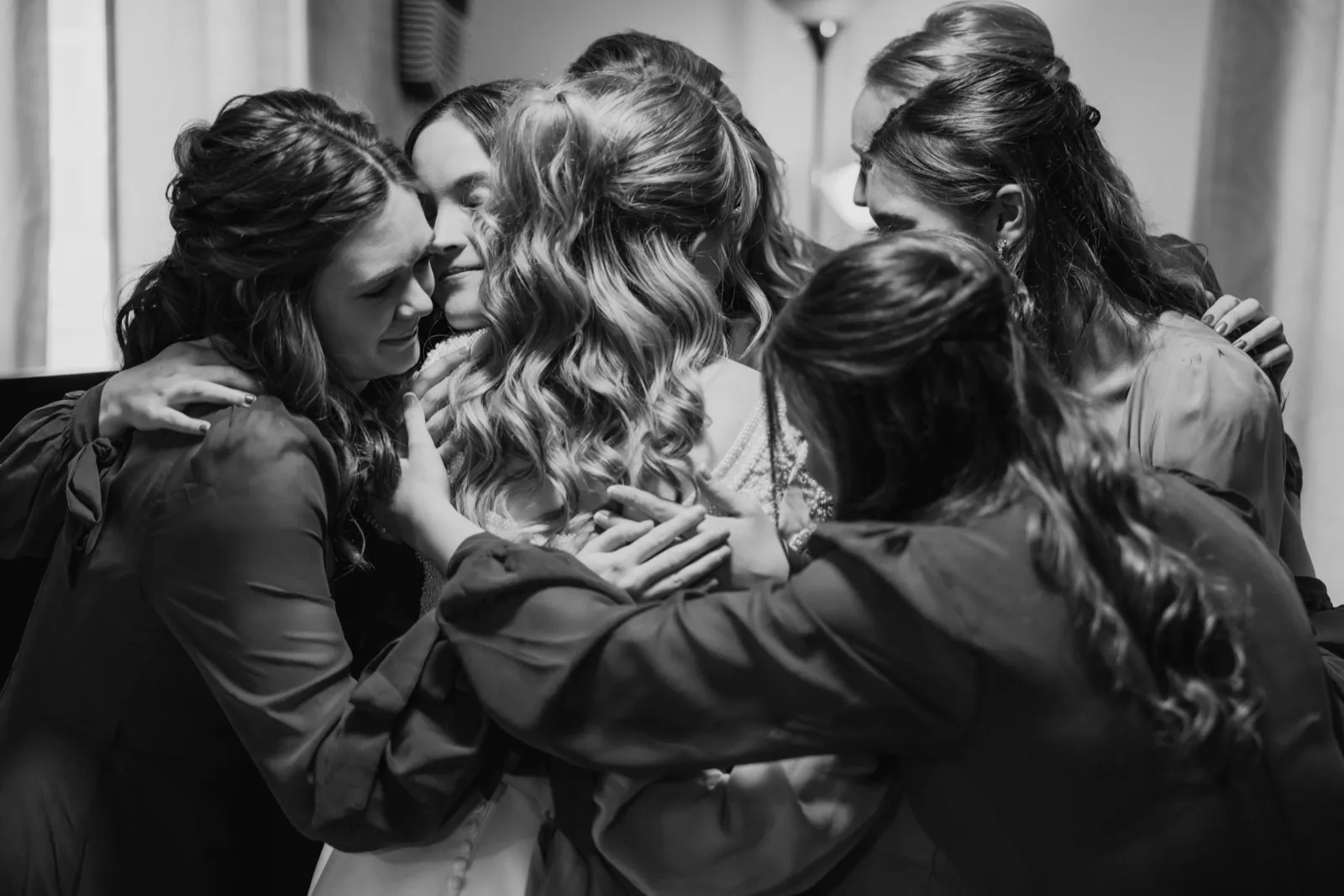 A bride stands surrounded by her bridesmaids in a tight group embrace, heads pressed together in a quiet moment before the ceremony — Tim Larsen Photography, Brainerd Lakes MN