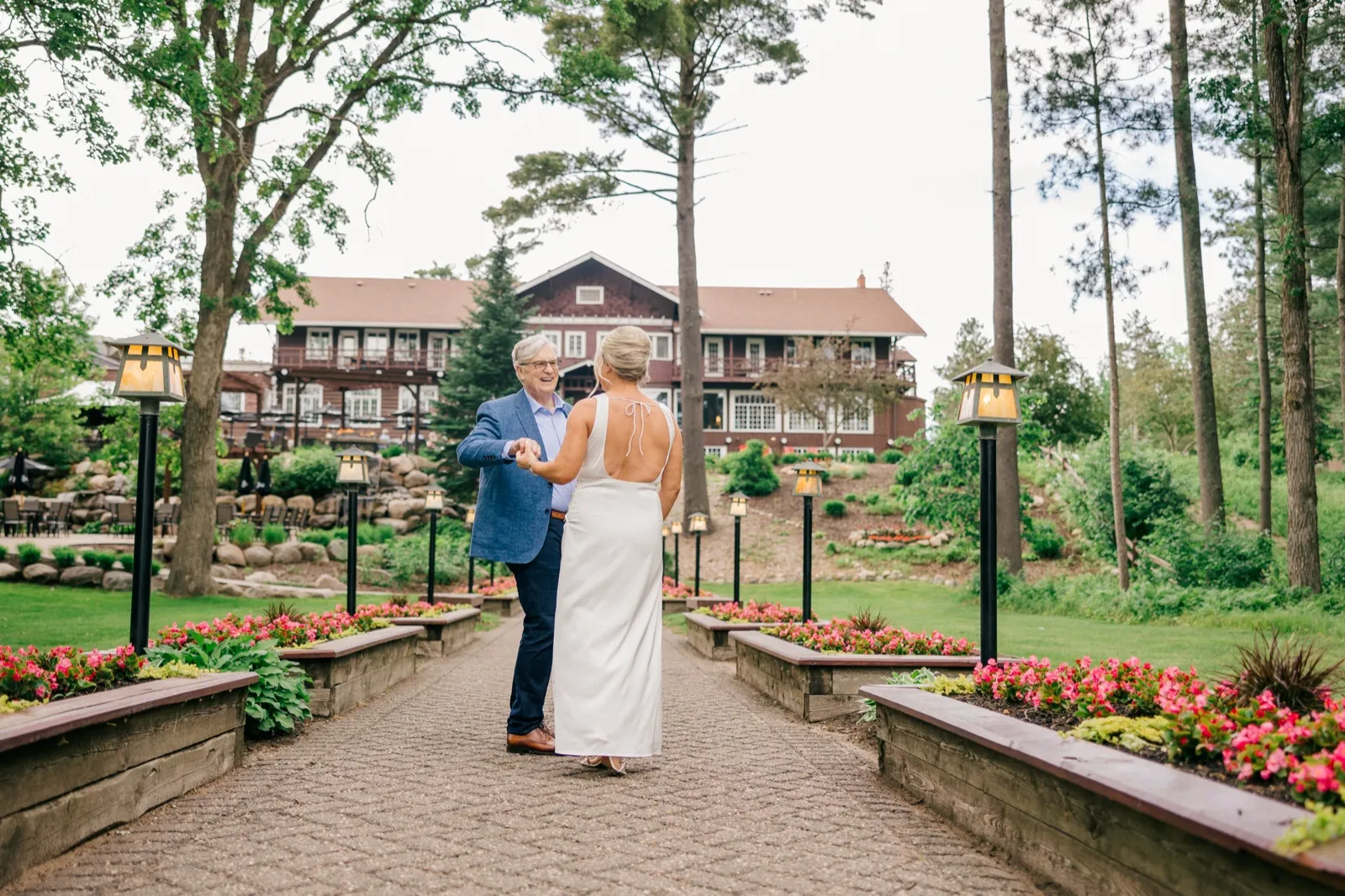 The bride and her father hold hands and smile at each other on a symmetrical lantern-lined garden path leading to the historic Grand View Lodge — Tim Larsen Photography, Brainerd Lakes MN