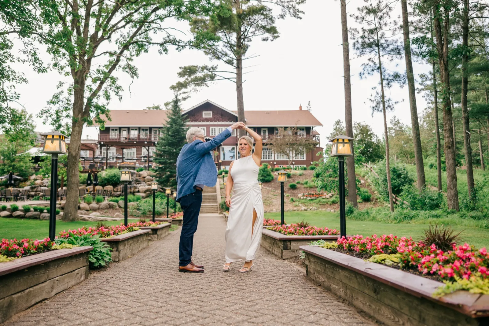 The groom twirls the bride on a symmetrical lantern-lined cobblestone path with the historic Grand View Lodge rising behind them — Tim Larsen Photography, Brainerd Lakes MN