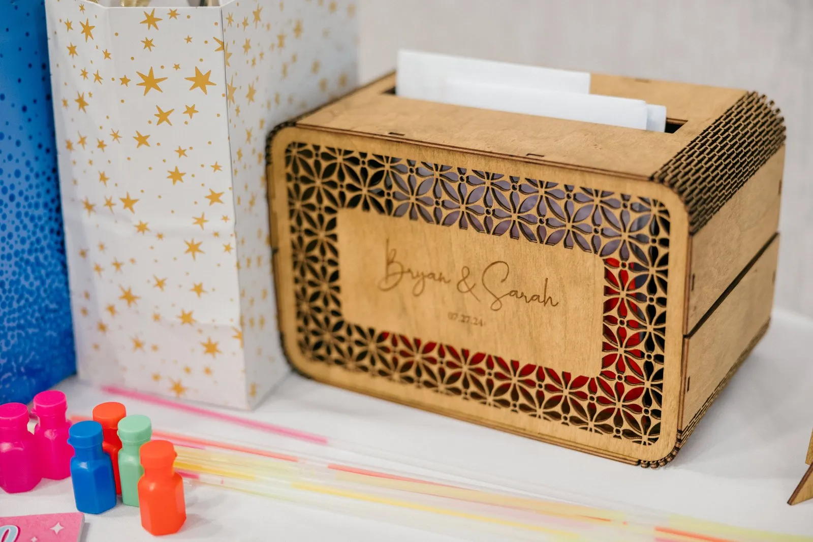 A laser-cut wooden card box engraved 'Bryan & Sarah 07.27.24' rests on a reception table beside envelopes and a small white floral arrangement at Grand View Lodge — Tim Larsen Photography, Brainerd Lakes MN