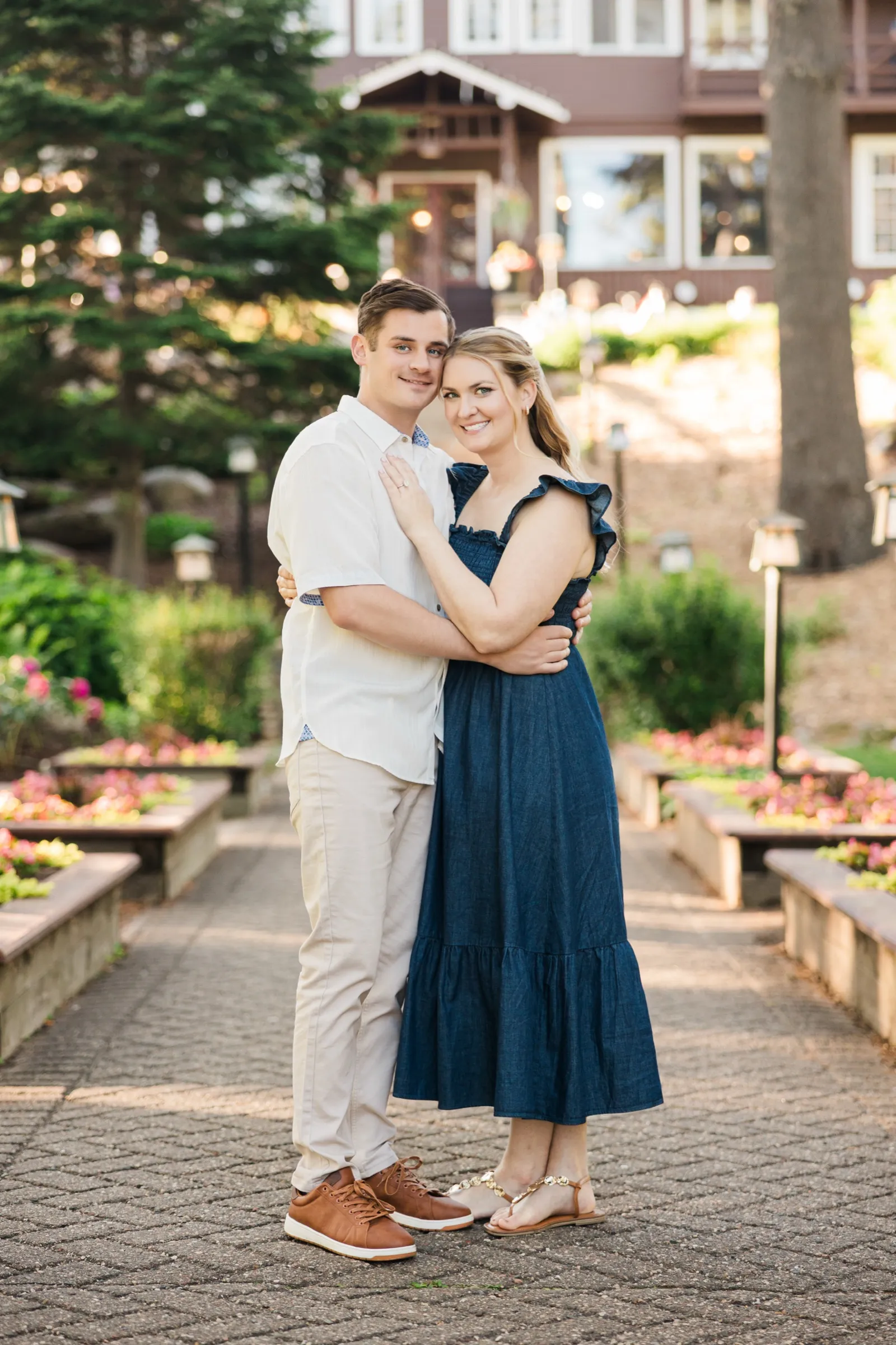 An engaged couple stand on the symmetrical flower-garden staircase at the historic Grand View Lodge, the lodge rising behind them — Tim Larsen Photography