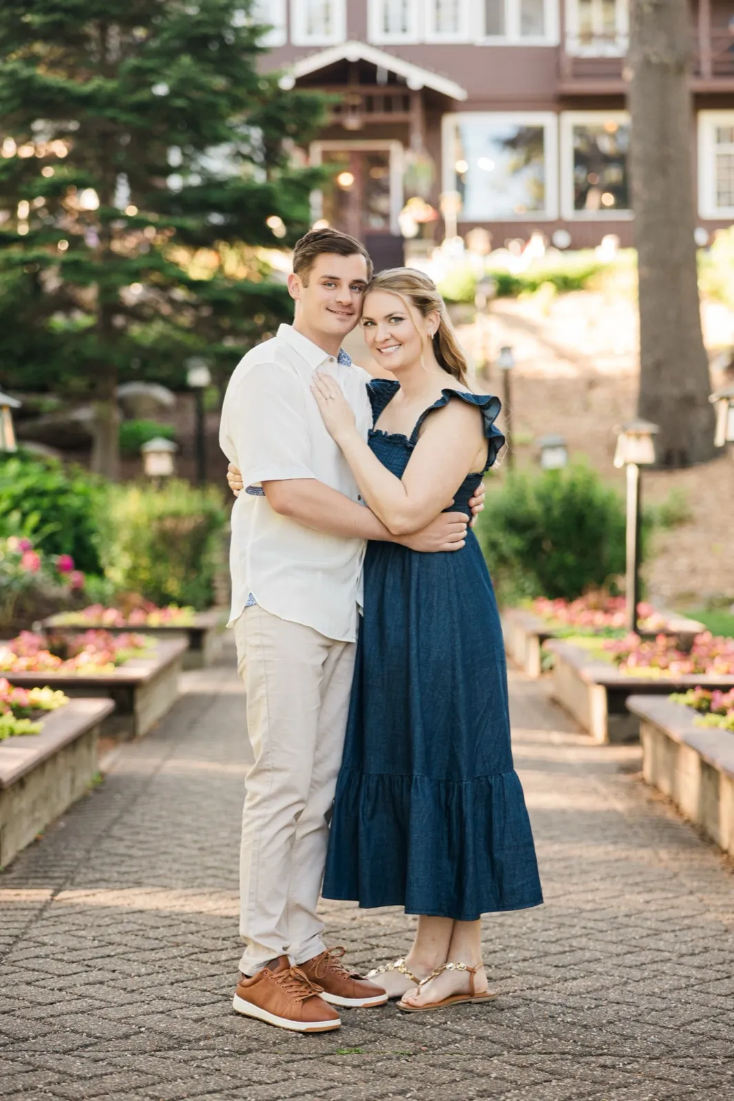 An engaged couple stand on the symmetrical flower-garden staircase at the historic Grand View Lodge, the lodge rising behind them — Tim Larsen Photography