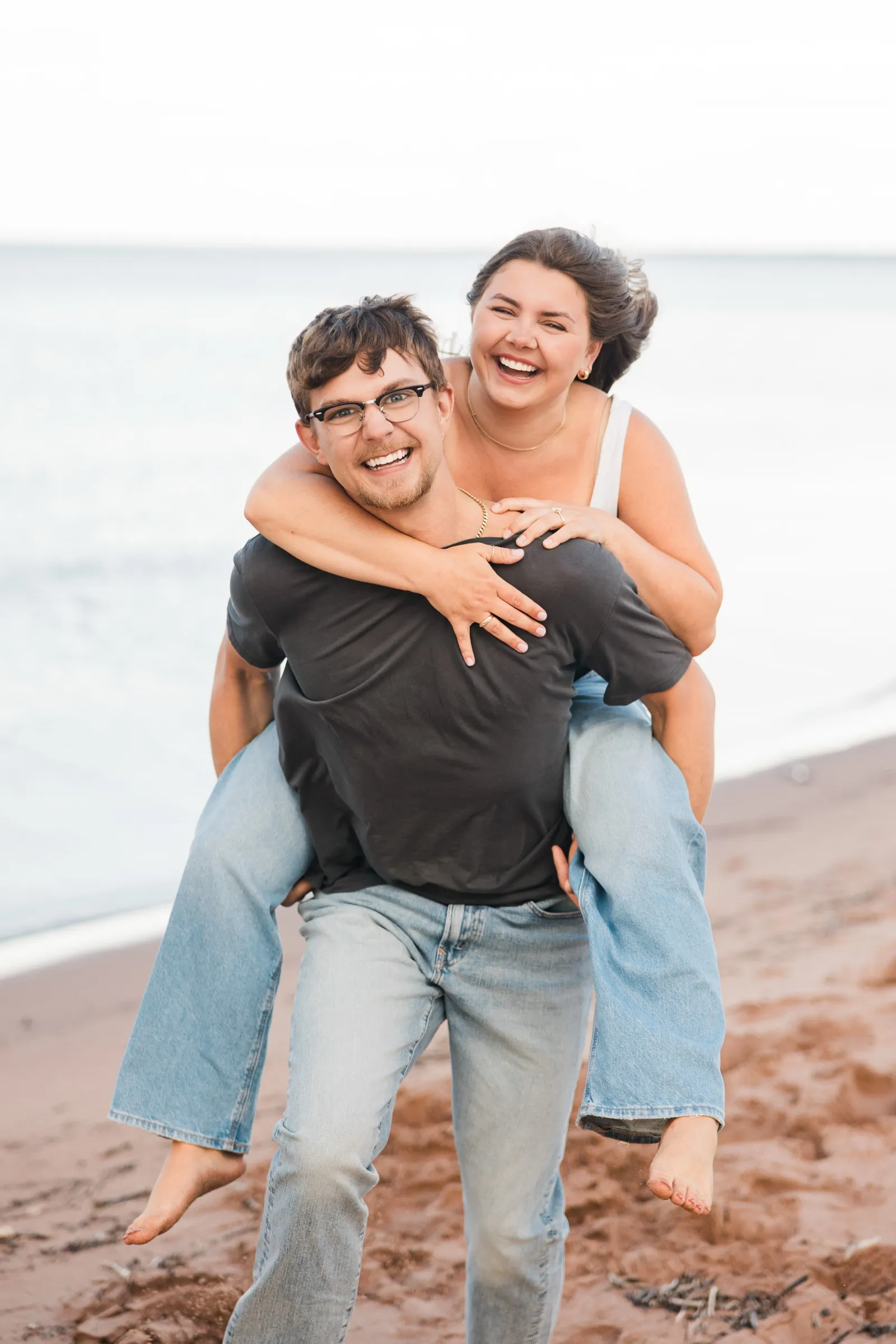 Jacklyn rides piggyback on Reeden as they both grin at the camera on the Lake Superior beach — Tim Larsen Photography