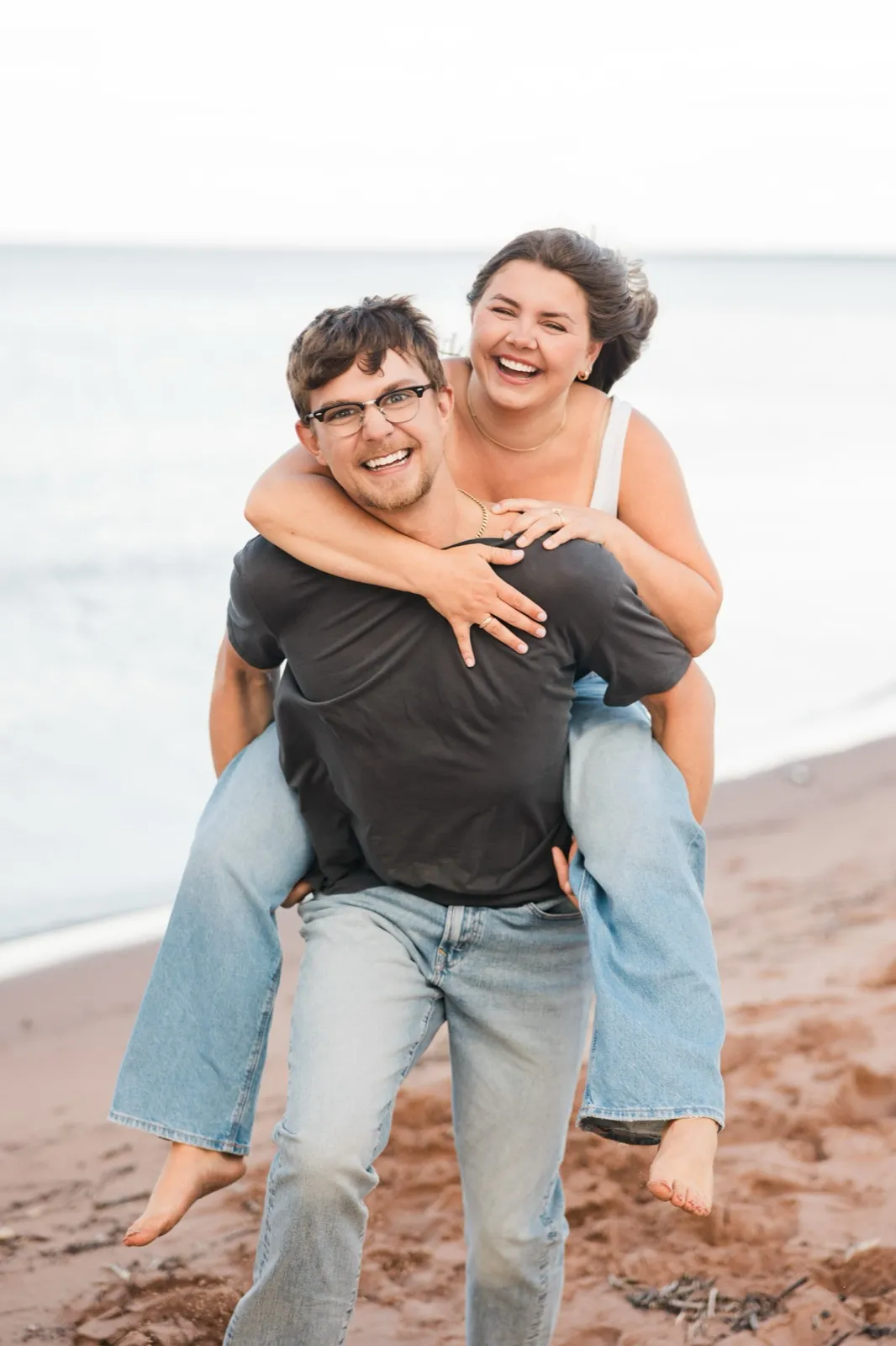 Jacklyn rides piggyback on Reeden as they both grin at the camera on the Lake Superior beach — Tim Larsen Photography