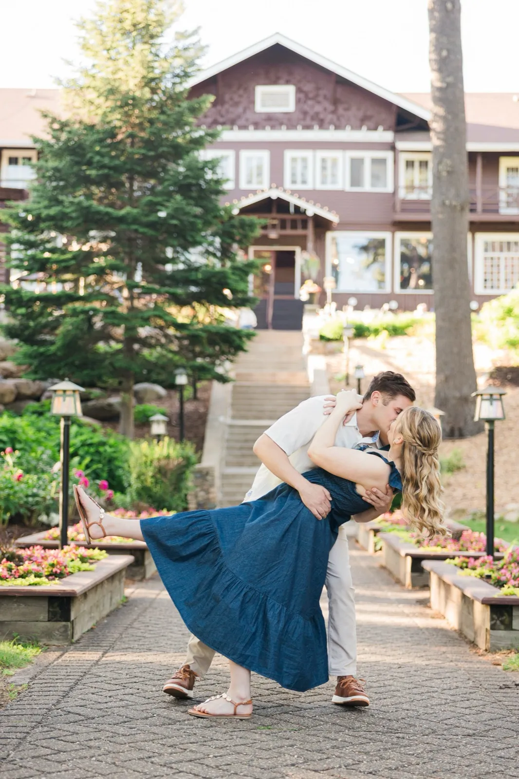 A man dips his fiancee into a kiss on the flower-garden staircase, the full historic Grand View Lodge rising behind them — Tim Larsen Photography