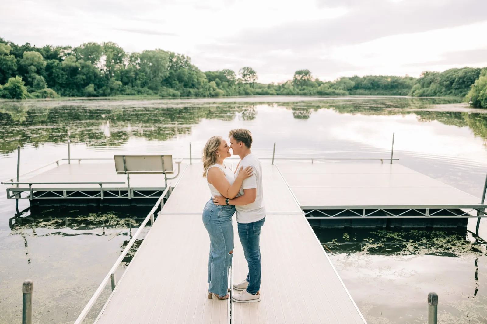 Abby and Anthony kiss at the end of a dock on Lake Auburn, the still water and tree line mirrored behind them — Tim Larsen Photography