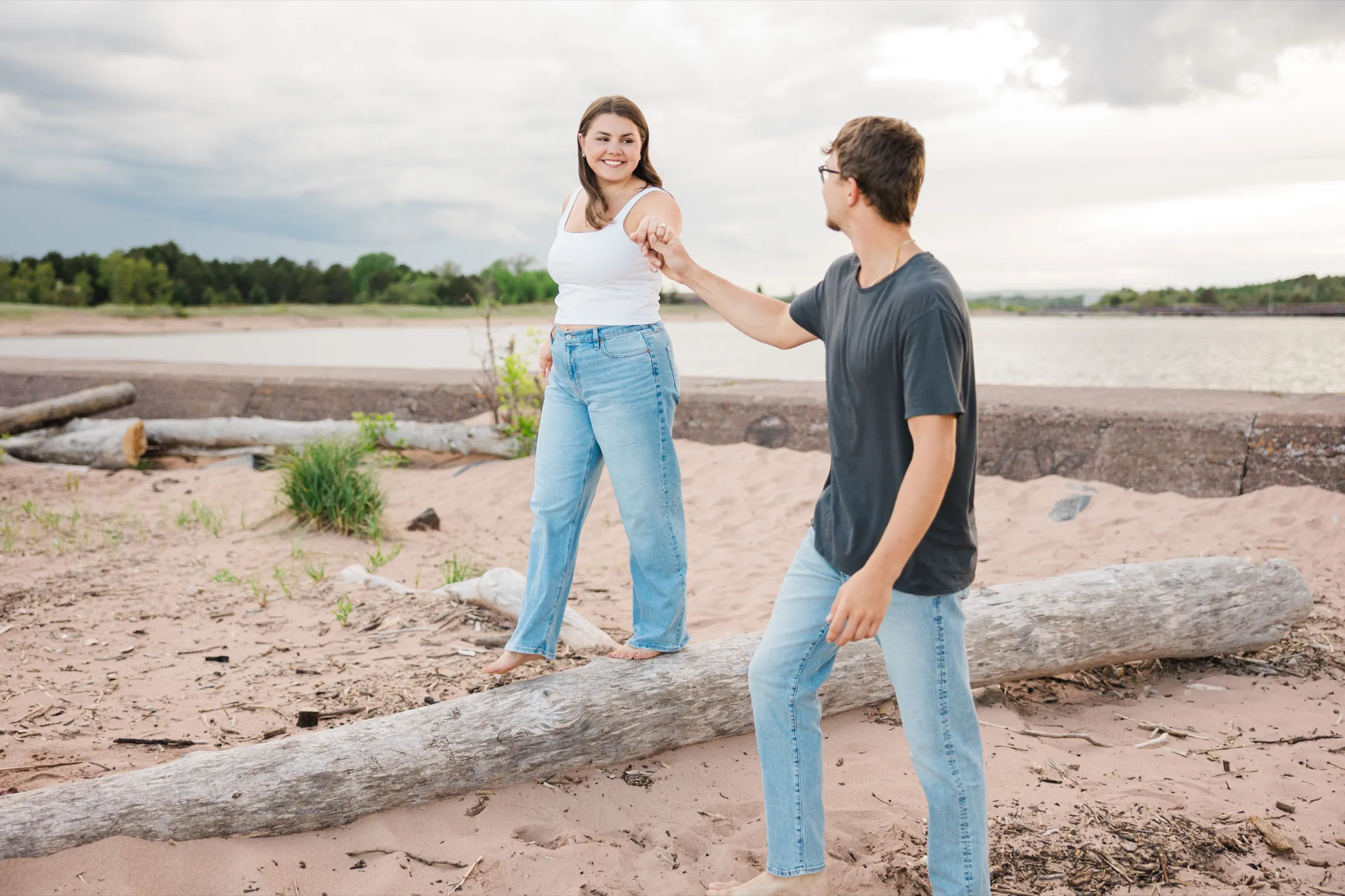 Jacklyn balances along a driftwood log holding Reeden's hand for support, a lagoon behind them — Tim Larsen Photography