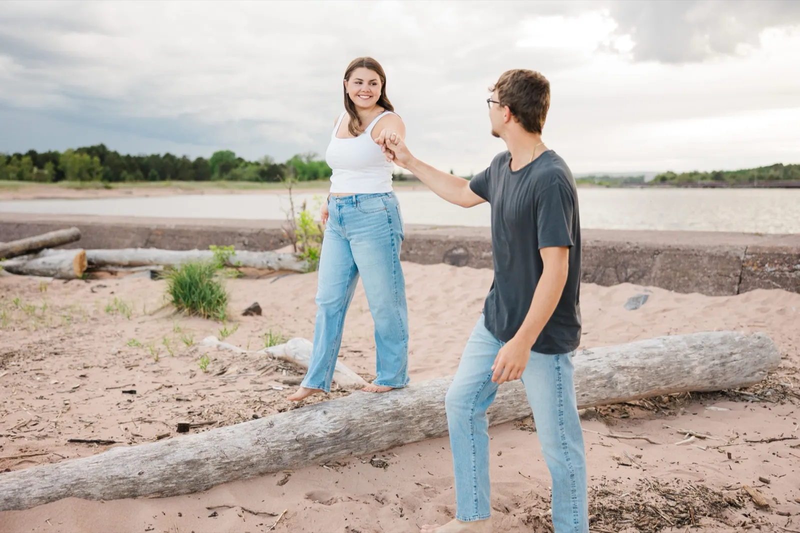 Jacklyn balances along a driftwood log holding Reeden's hand for support, a lagoon behind them — Tim Larsen Photography