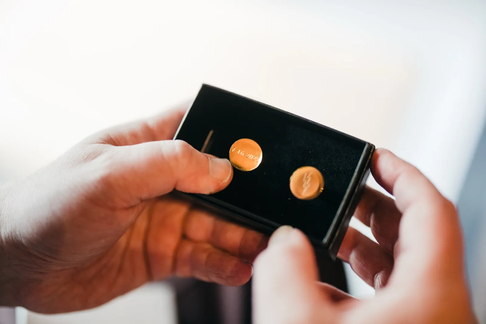Two pairs of hands hold open a small black box revealing a pair of engraved gold cufflinks, one stamped with a date and the other with an initial. — Tim Larsen Photography, Brainerd Lakes MN
