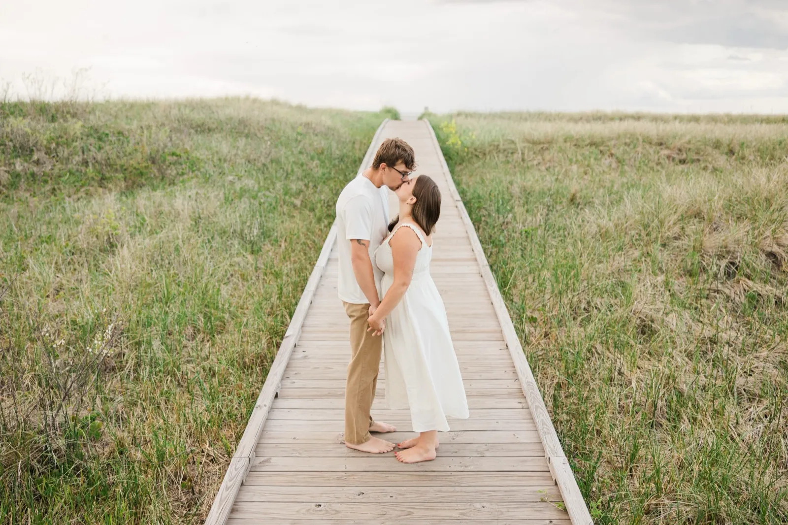Reeden kisses Jacklyn's forehead on the long boardwalk that runs through the dune grass toward the beach — Tim Larsen Photography