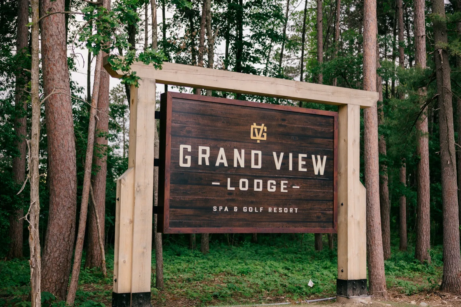 The carved wooden Grand View Lodge Spa & Golf Resort entrance sign standing among tall pines on a June afternoon — Tim Larsen Photography, Brainerd Lakes MN