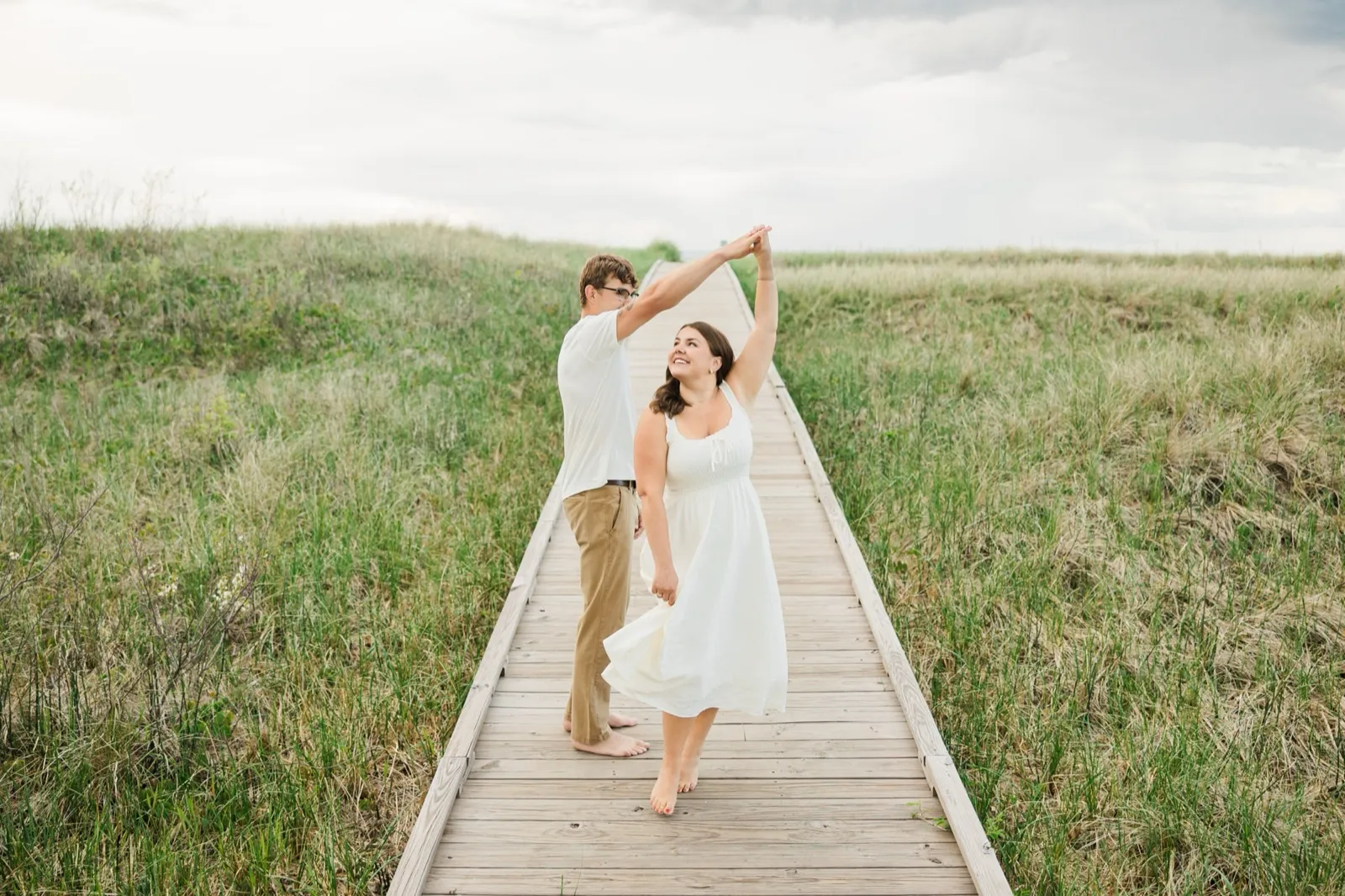 Reeden twirls Jacklyn on the dune boardwalk, her white dress and hair swinging out as she smiles — Tim Larsen Photography