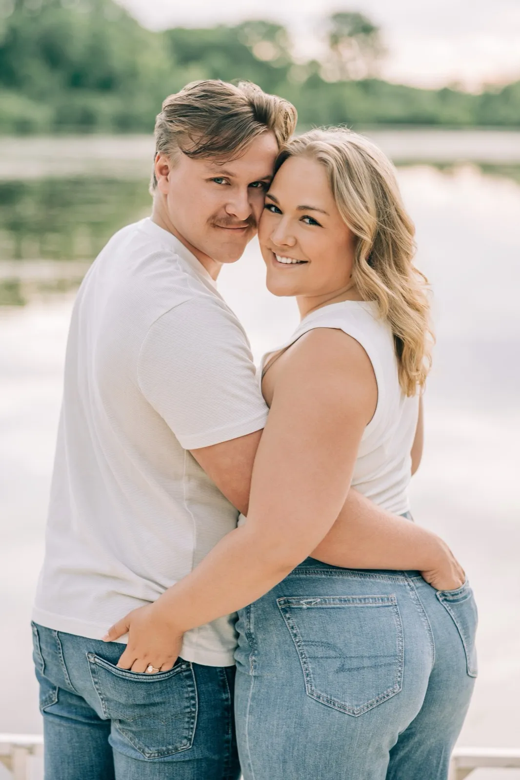 Abby and Anthony sit barefoot at the edge of the dock with their feet over the water as he leans into her — Tim Larsen Photography