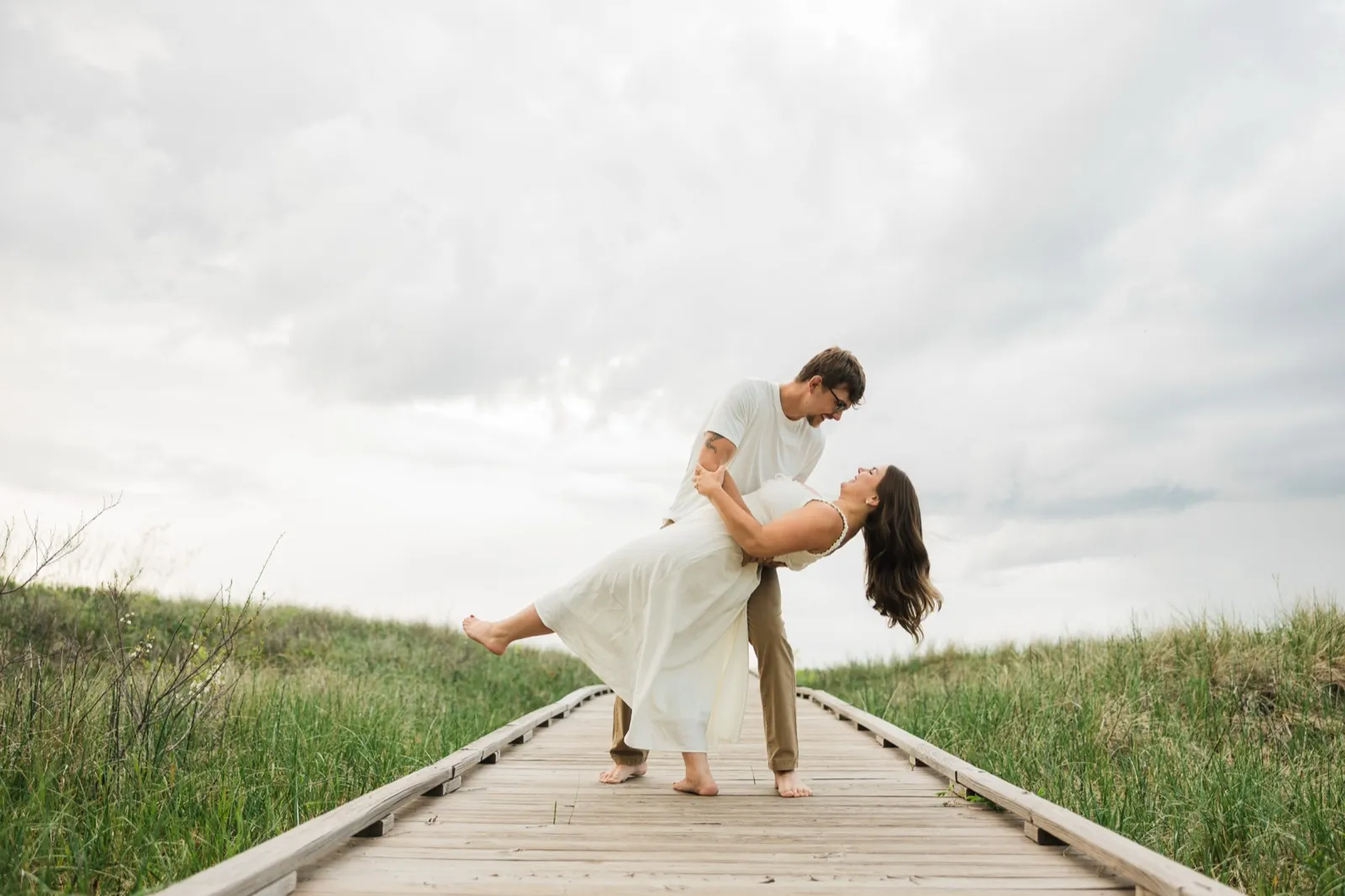 Reeden dips Jacklyn backward on the dune boardwalk against a wide, dramatic sky — Tim Larsen Photography