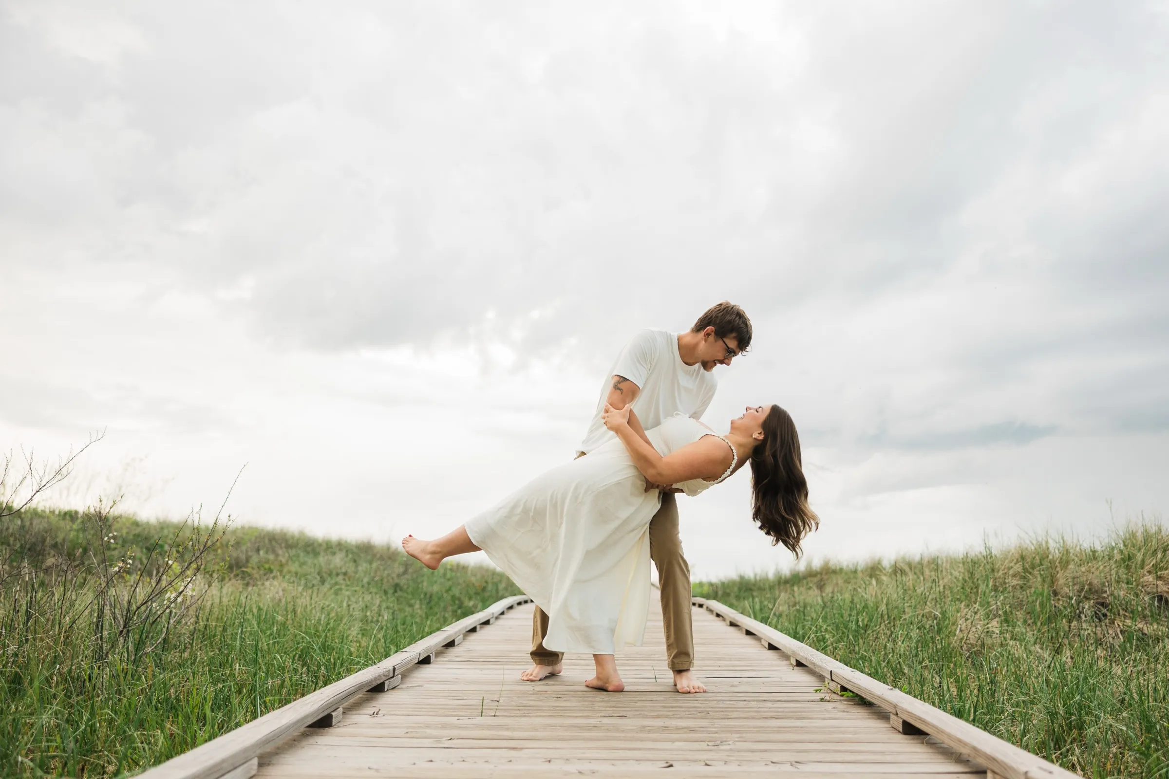 Reeden dips Jacklyn backward on the dune boardwalk against a wide, dramatic sky — Tim Larsen Photography