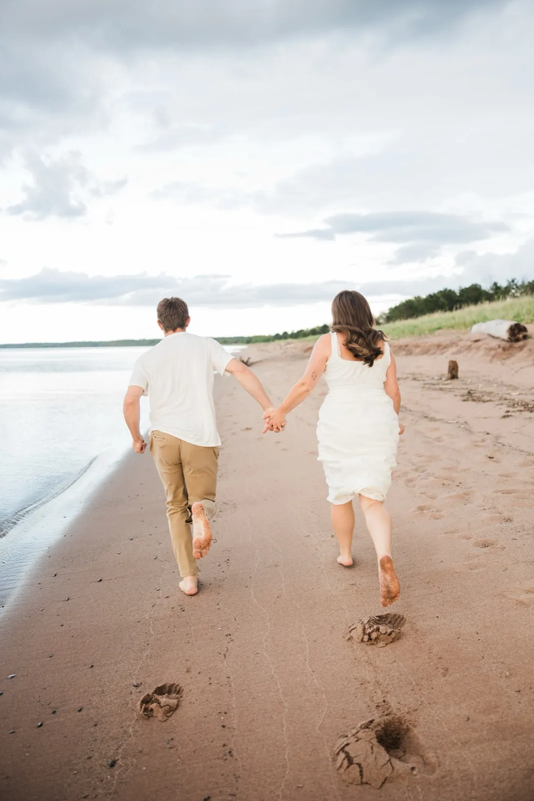 Reeden and Jacklyn run hand in hand down the long Lake Superior beach, footprints trailing in the reddish sand — Tim Larsen Photography